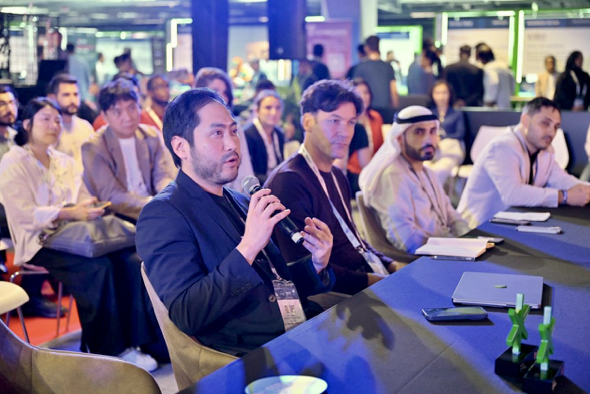 Han Gust, part of the judge panel, speaking at the DMCC x AGCC Global AI Competition Sustainability Edition at Expand North Star 2024, with an engaged audience in the background.