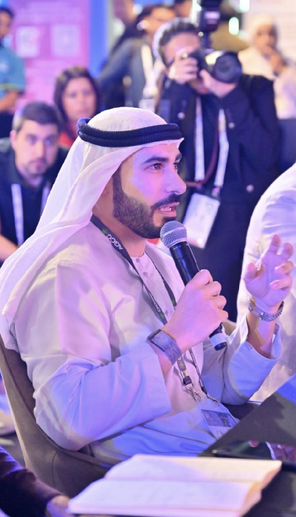 Salman Amiri serving as a judge, holding a microphone and engaged in evaluating AI pitches at the DMCC x AGCC Global AI Competition Sustainability Edition during Expand North Star 2024.